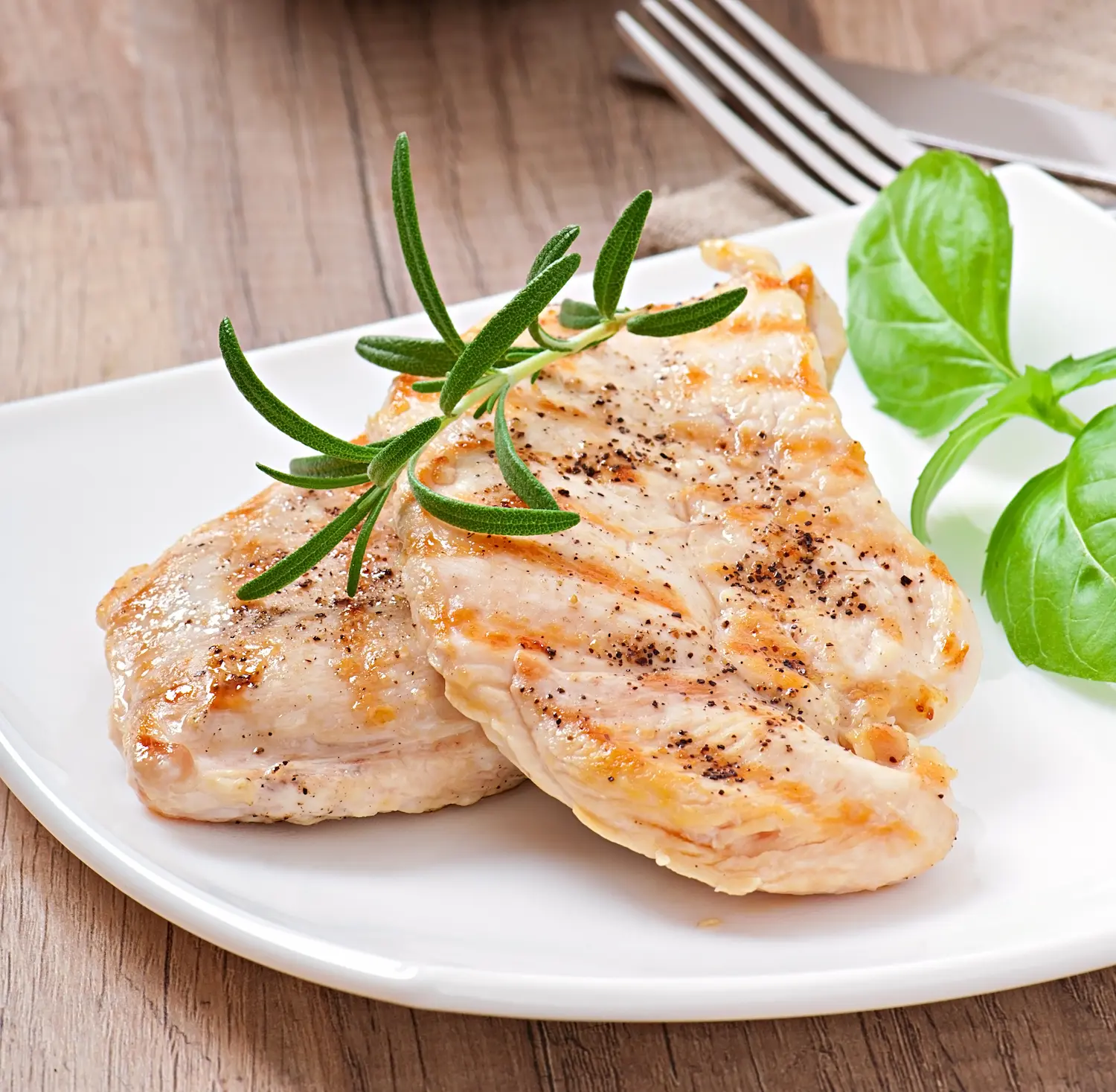 Cooked chicken breasts sliced on a wooden board with small bowls of spices nearby