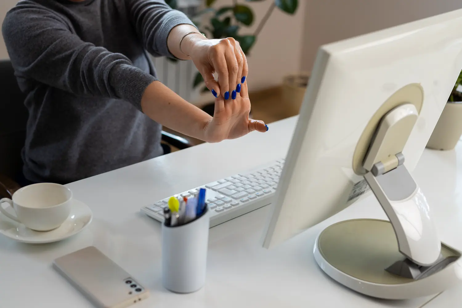 A desk worker gently stretching their wrist and fingers to relieve tension.