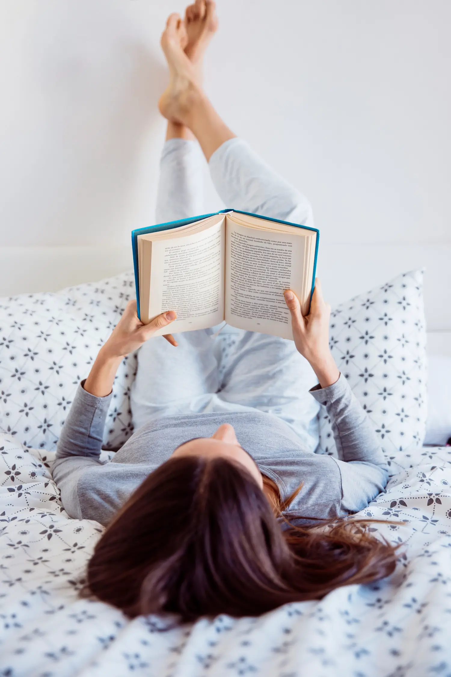 Woman in pajamas reading a book in bed, phone face down on the nightstand for a digital detox
